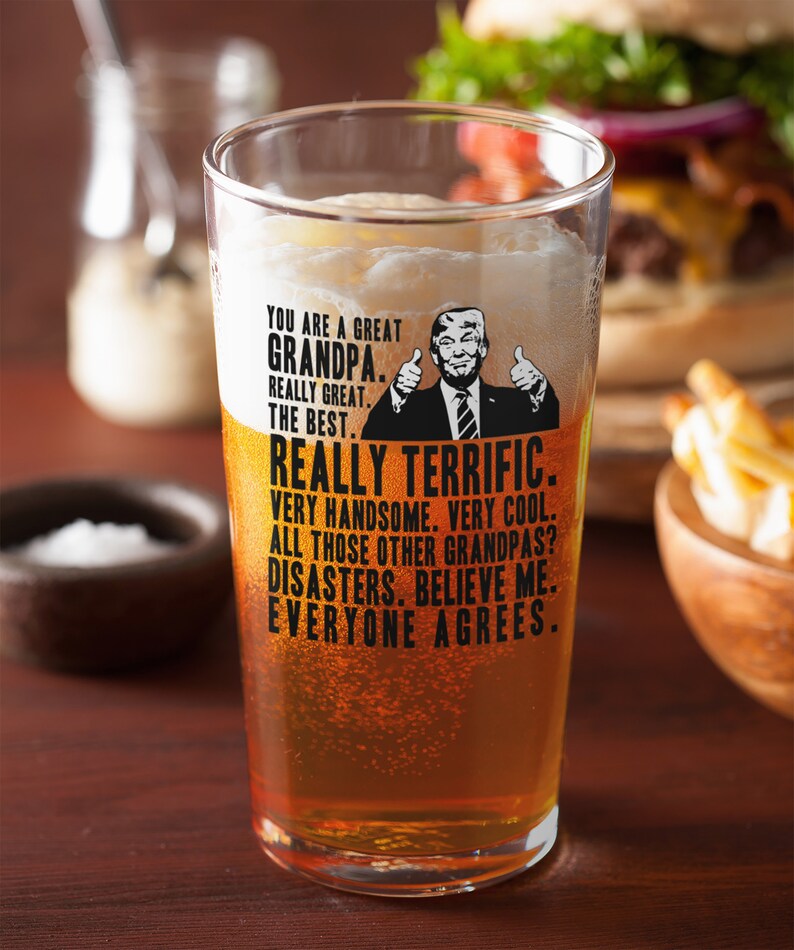 May include: A clear glass beer mug with a humorous message about a grandpa. The message reads "You are a great grandpa. Really great. The best. Really terrific. Very handsome. Very cool. All those other grandpas? Disasters. Believe me. Everyone agrees."