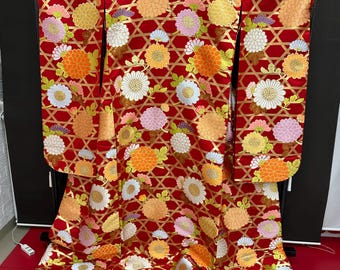 May include: A red kimono with a gold and white floral pattern. The kimono is decorated with a repeating pattern of chrysanthemums and a lattice design.