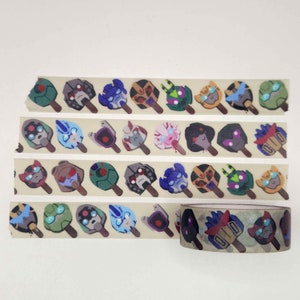 May include: A roll of washi tape with a repeating pattern of cartoon robot heads on popsicle sticks. The tape is beige with brown popsicle sticks and colorful robot heads. The tape is partially unrolled, showing the pattern.