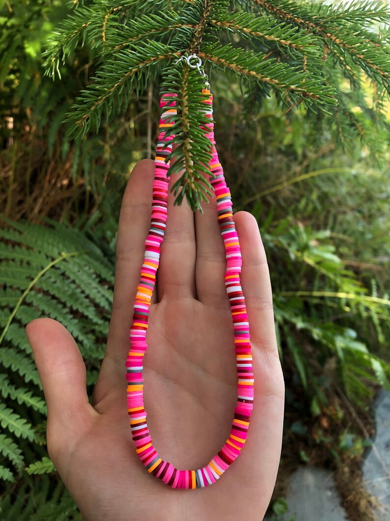 K&ouml;nnte beinhalten: Eine bunte Perlenkette mit rosa, orange, wei&szlig;en und grauen Perlen. Die Kette besteht aus runden, flachen Perlen.