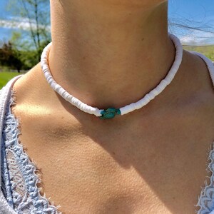 May include: A white shell choker necklace with a turquoise stone accent.