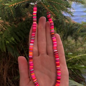 K&ouml;nnte beinhalten: Eine bunte Perlenkette mit rosa, orange, wei&szlig;en und grauen Perlen. Die Kette besteht aus runden, flachen Perlen, die &uuml;bereinander gestapelt sind.