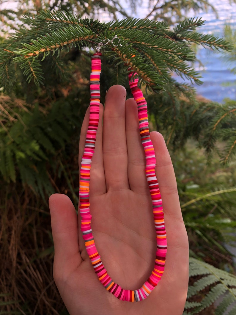 K&ouml;nnte beinhalten: Eine bunte Perlenkette mit rosa, orange, wei&szlig;en und grauen Perlen. Die Kette besteht aus runden, flachen Perlen, die &uuml;bereinander gestapelt sind.
