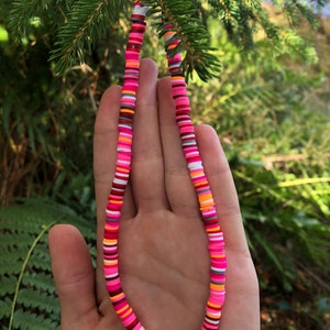 K&ouml;nnte beinhalten: Eine bunte Halskette aus runden Perlen in Pink, Orange, Wei&szlig; und Grau. Die Halskette besteht aus verschiedenen Farben und Mustern.