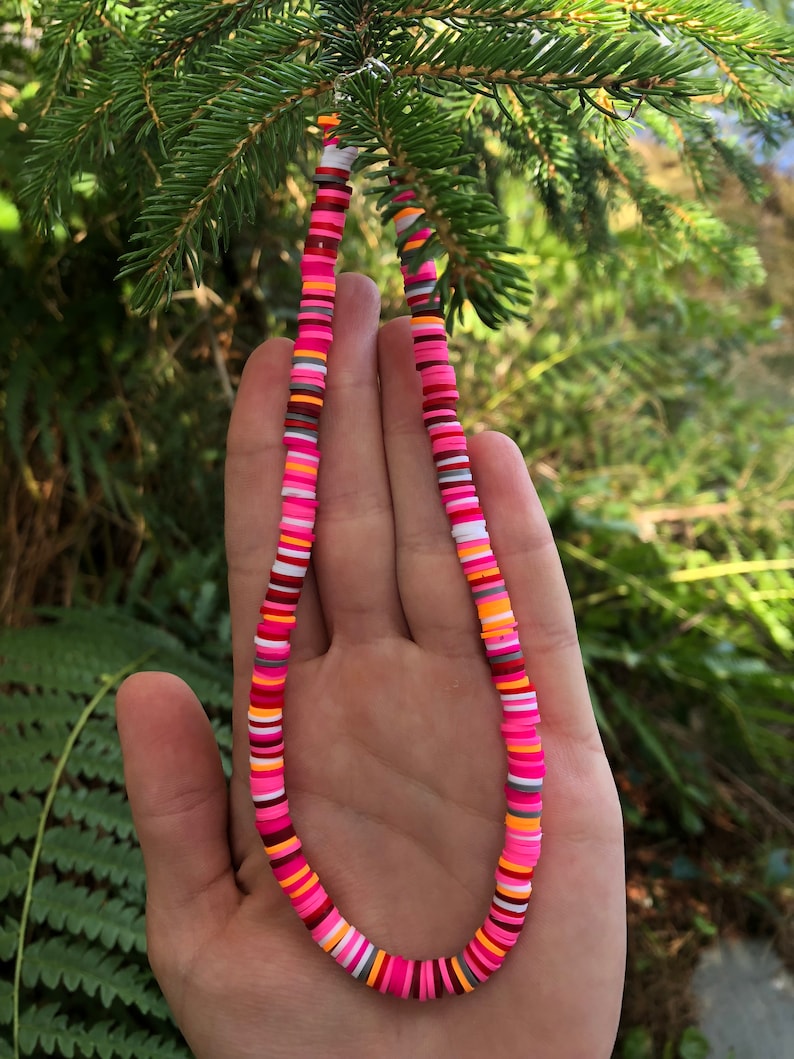 K&ouml;nnte beinhalten: Eine bunte Halskette aus runden Perlen in Pink, Orange, Wei&szlig; und Grau. Die Halskette besteht aus verschiedenen Farben und Mustern.
