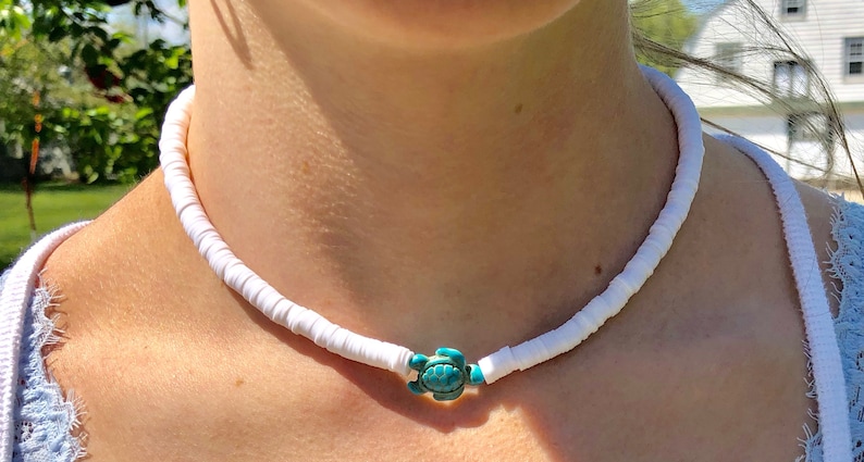 May include: A white shell necklace with a turquoise turtle charm.