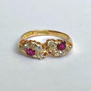 Puede incluir: Un anillo de oro con dos rubíes y diamantes más pequeños engastados en un delicado diseño floral.