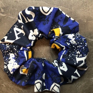 May include: Blue and yellow patterned scrunchie with white lettering. The lettering says "MASON" and "LA"