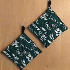 May include: Two green and white pot holders with the New York Jets logo and the words "Jets" and "Football" repeated on them.
