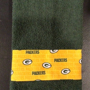 May include: Green towel with a yellow band featuring the Green Bay Packers logo and the word "Packers" repeated multiple times.