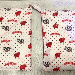 May include: Two square pot holders with a white background, red polka dots, and a repeating pattern of the word "Badgers" and the Wisconsin "W" logo. Each pot holder has a red trim and a hanging loop.