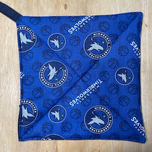 May include: Blue and white pot holder with a repeating pattern of basketballs and the Minnesota Timberwolves logo. The logo features a wolf howling at the moon with the words "Minnesota Timberwolves" around it.