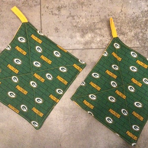 May include: Two green and yellow fabric pot holders with the word "Packers" repeated on them.