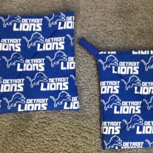 May include: Two blue and white pot holders with the Detroit Lions logo repeated on the fabric. The pot holders have a loop for hanging.