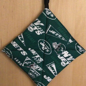 May include: Green and white pot holder with the New York Jets logo and the words "Jets" and "Football" repeated throughout.