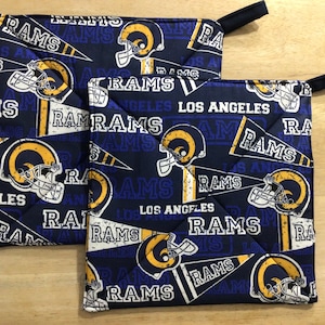 May include: Two blue and gold pot holders with a repeated pattern of the Los Angeles Rams logo and the words "Rams" and "Los Angeles".