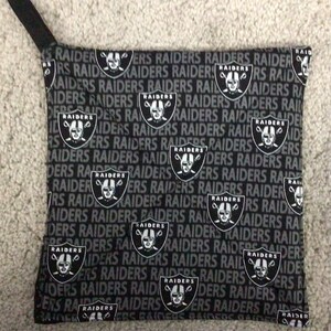 May include: Black and white fabric with a repeating pattern of the Oakland Raiders logo and the word "RAIDERS".