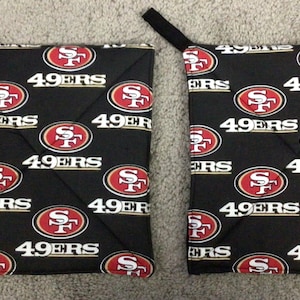 May include: A pair of black pot holders with a red and white San Francisco 49ers logo pattern.