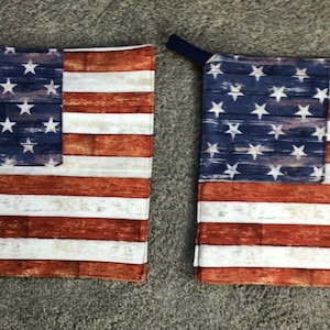 May include: A pair of red, white, and blue American flag oven mitts. The mitts are made of fabric and have a distressed woodgrain pattern.