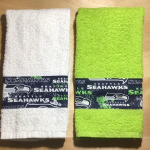 May include: Two towels, one white and one green, with a blue and white Seattle Seahawks themed border.