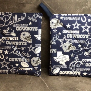May include: Two blue and white pot holders with a Dallas Cowboys theme. The pot holders feature a variety of Cowboys logos, including the star, the horseshoe, and the team's name.
