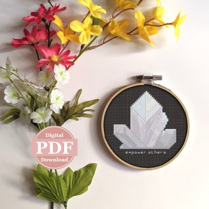 May include: A black embroidery hoop with a white crystal design and the text "empower others". The hoop is surrounded by yellow and pink flowers.