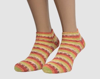 May include: A pair of ankle socks with horizontal stripes in shades of orange, green, and brown. The socks are worn on a person's feet, with the legs visible in the background. The socks have a ribbed cuff.