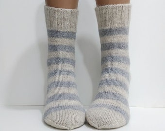 May include: A pair of knitted socks with a striped pattern in shades of gray and beige. The socks are ankle-length and have a ribbed cuff.