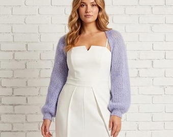 May include: A white dress with a high slit and a light purple, long-sleeved shrug. The dress has a square neckline and a fitted bodice. The shrug is made of a soft, fuzzy material.