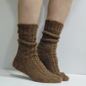 Könnte beinhalten: Ein Paar braune Stricksocken mit einem Zopfmuster. Die Socken sind aus einem weichen, warmen Material gefertigt und perfekt für kaltes Wetter.
