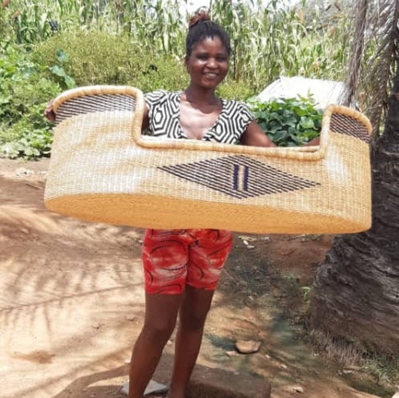 May include: A woman holds a large, woven basket with a diamond pattern in black and blue. The basket is made of natural materials and has a light brown color.