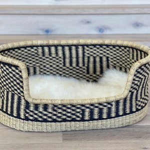 May include: A black and white woven dog bed with a white faux fur liner. The bed is oval shaped and has a raised rim.