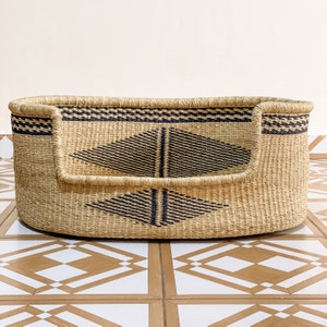 May include: A woven pet bed with a black and tan diamond pattern. The bed is oval shaped and has a raised rim.