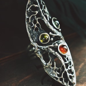 May include: A silver ring with a tree design and four colorful gemstones. The ring is on a wooden surface.