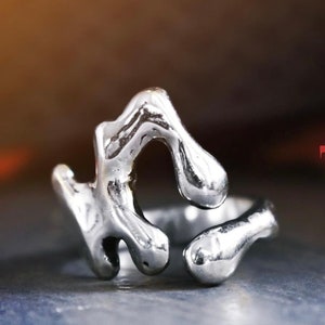 May include: A silver ring with an abstract, organic design. The ring is made of smooth, polished metal and has a unique, modern look.