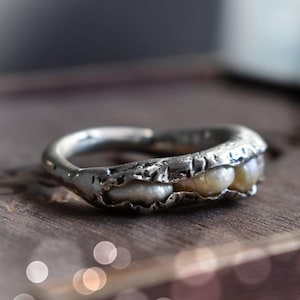 Peut inclure: Une bague en argent avec une bande texturée et trois perles blanches serties dans la bande.