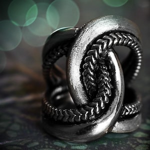 May include: A silver ring with a braided design. The ring is made of multiple intertwined bands, creating a complex and intricate pattern.