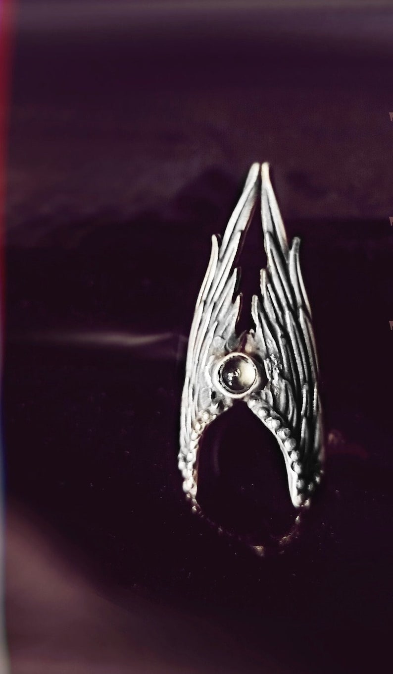 May include: A silver ring featuring a clear gemstone set in the centre, shaped like two wings meeting.