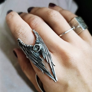 May include: A silver ring featuring a detailed wing design with a small, clear gemstone at its centre.