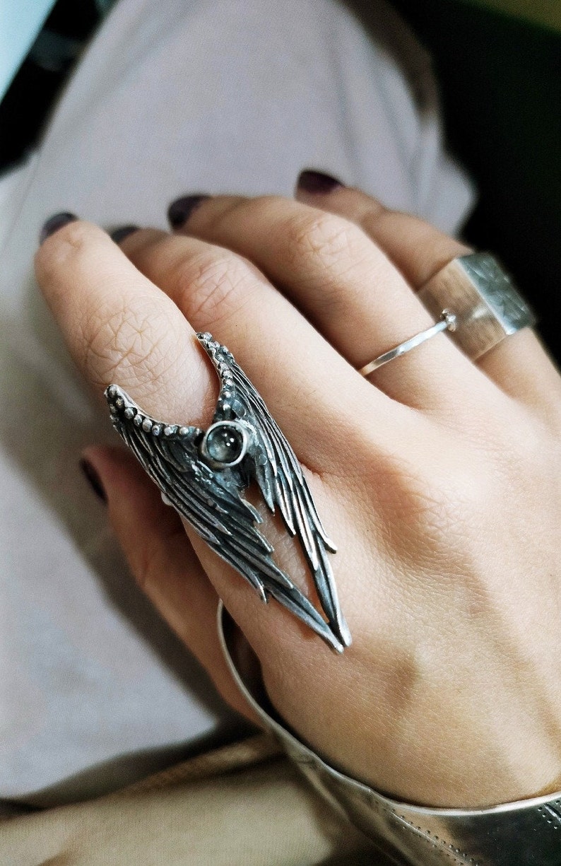 May include: A silver ring featuring a detailed wing design with a small, clear gemstone at its centre.