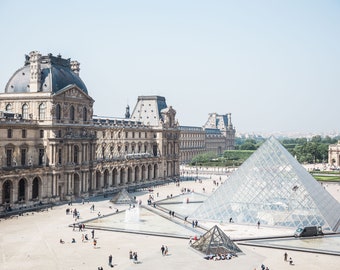 May include: An aerial view of the Louvre Museum in Paris, France. The iconic glass pyramid stands in the courtyard, surrounded by a large plaza and the museum's historic facade.