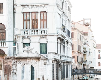 May include: A white building with arched windows and a stone archway overlooking a narrow canal in Venice, Italy. A small boat is docked in the canal.