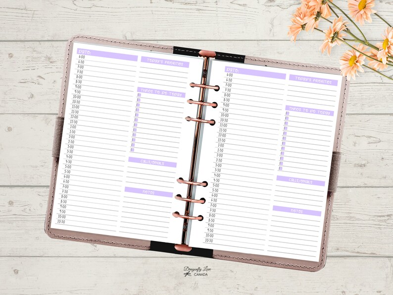 May include: Open planner with a light pink cover and rose gold rings. The pages are white with a purple header and lines for scheduling. Sections include "Today's Priorities", "Things to Do Today", "Calls/Emails", and "Notes". The planner is open to a double-page spread.