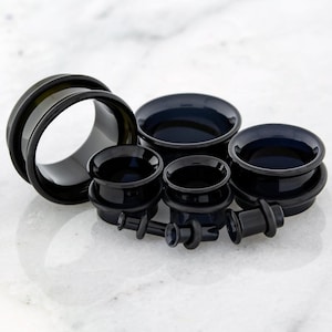 May include: A collection of black ear gauges in various sizes. The gauges are made of a glossy material and have a smooth, rounded design. The collection includes several tunnel and plug styles.