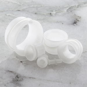 Puede incluir: Una colección de expansores y tapones para las orejas blancos y translúcidos en varios tamaños y estilos. El surtido incluye tapones de túnel, tapones de doble ensanchamiento y algunas piezas más pequeñas, todas hechas de un material liso y mate.