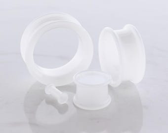 May include: A collection of translucent white ear gauges in various sizes. The set includes two large tunnel plugs, a smaller tunnel plug, and a small barbell-style plug. The gauges are made of a smooth, possibly acrylic, material.