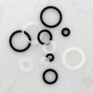 May include: An assortment of black and white rubber O-rings of varying sizes. The O-rings are circular and appear to be made of a flexible material. The sizes range from small to large, with a mix of solid black and translucent white rings.