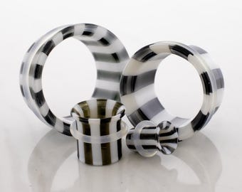May include: Four pieces of body jewelry, including two large ear gauges, a small plug, and a small tunnel. The jewelry features a black and white striped pattern. The pieces are made of a translucent material and are arranged on a white surface.