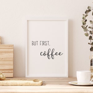Puede incluir: Una impresión enmarcada en blanco con el texto "BUT FIRST, coffee" en fuente cursiva negra. La impresión está sobre una encimera de madera con una taza de café blanca, una tabla de cortar de madera y un jarrón con ramas de eucalipto.
