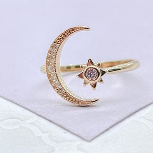 Könnte beinhalten: Ein goldfarbener Ring mit einem Mond-Design, besetzt mit kleinen, klaren Steinen. Ein Stern mit einem zentralen klaren Stein befindet sich neben dem Mond. Der Ring ist vor einem hellen Hintergrund platziert.